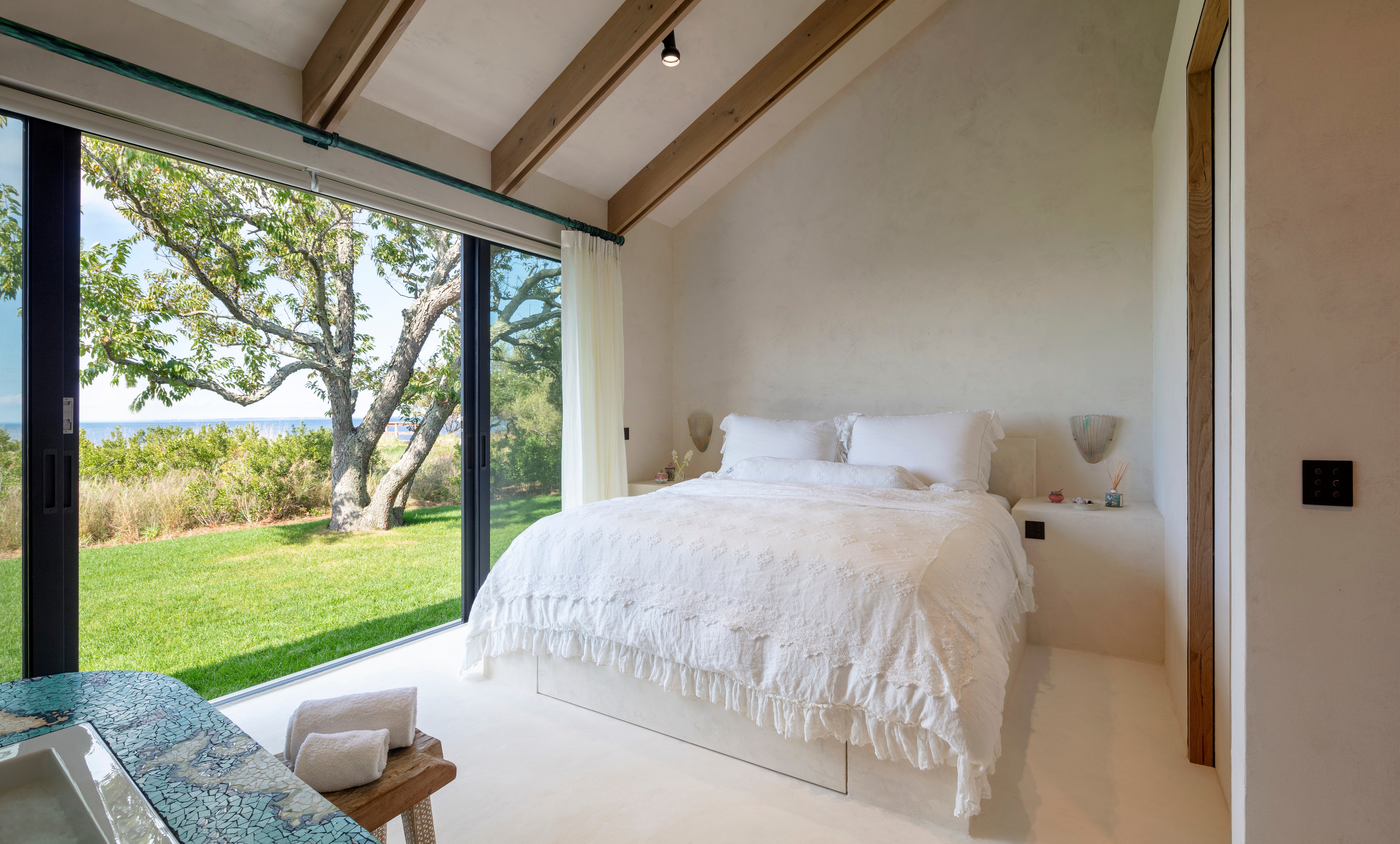 A bedroom photographed in the afternoon with daylight streaming in from a sliding glass door along the wall. 