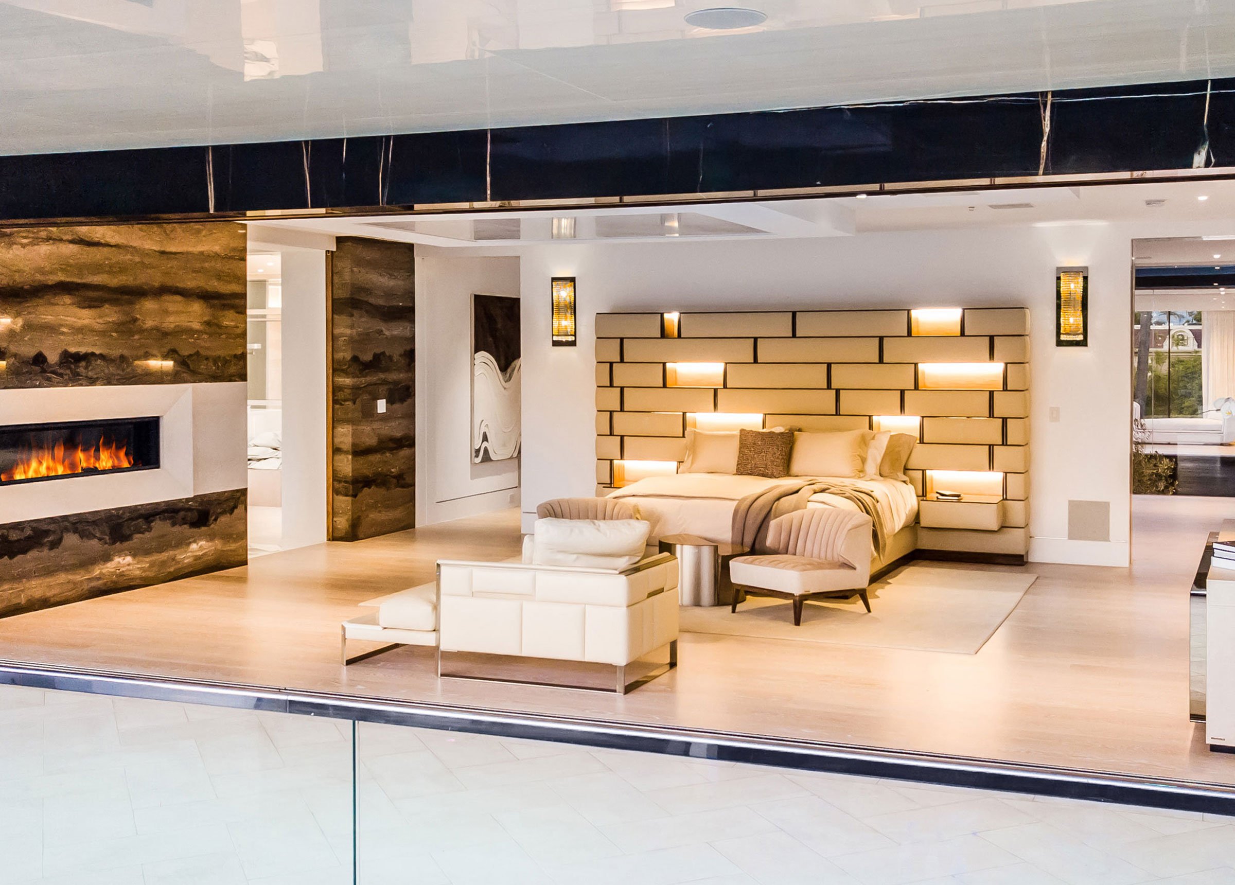 From the outside of a window looking in on a bedroom with warm white accent lights and modern architectural details.